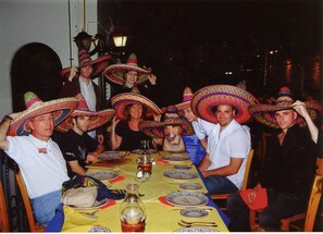Un groupe de personnes est assis autour d’une table recouverte d’une nappe jaune, avec des assiettes et des verres.