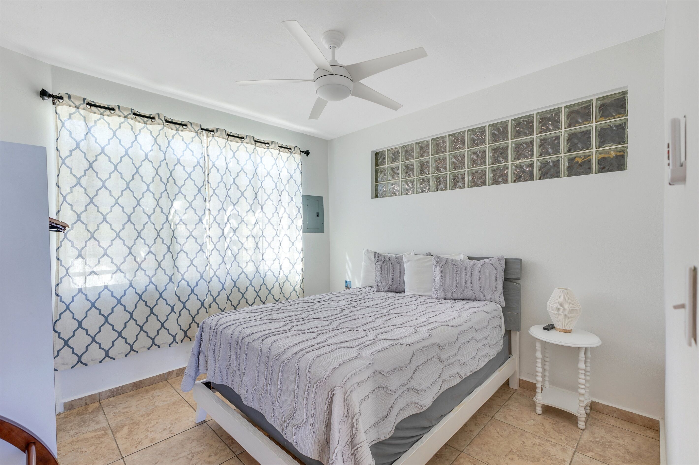 Una camera da letto con un letto, una ventola a soffitto, una finestra con vista e un comodino con una lampada.