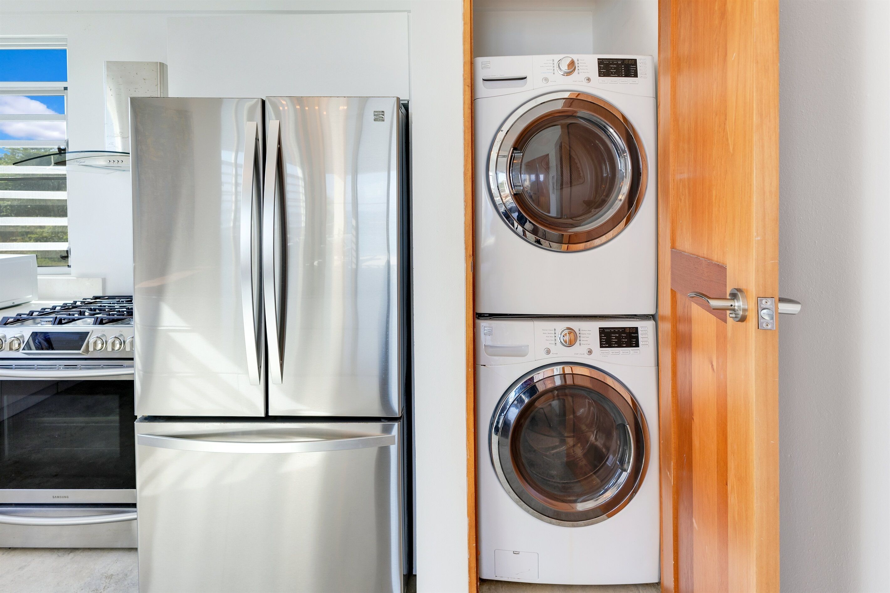 Une cuisine compacte équipée d’un réfrigérateur en acier inoxydable, d’un four encastré et d’un lave-linge.