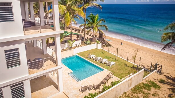 A modern building with a pool, beach view, and palm trees. - "Seas the Day" at Sandy Beach (Rincon)