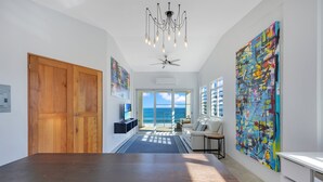 A spacious hallway with a wooden door, a ceiling fan, and a large abstract painting on the wall. - "Seas the Day" at Sandy Beach (Rincon)