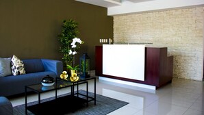 A modern living room with a blue sofa, a glass coffee table, and a reception desk against a stone wall.