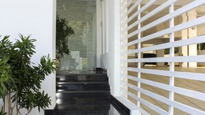 A modern staircase with black steps leading to a glass door, flanked by white railings and potted plants.