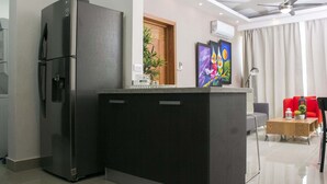 A modern kitchen with a built-in refrigerator, a wooden door, and a small island with a sink. There is a dining area with a table and chairs, and a ceiling fan.
