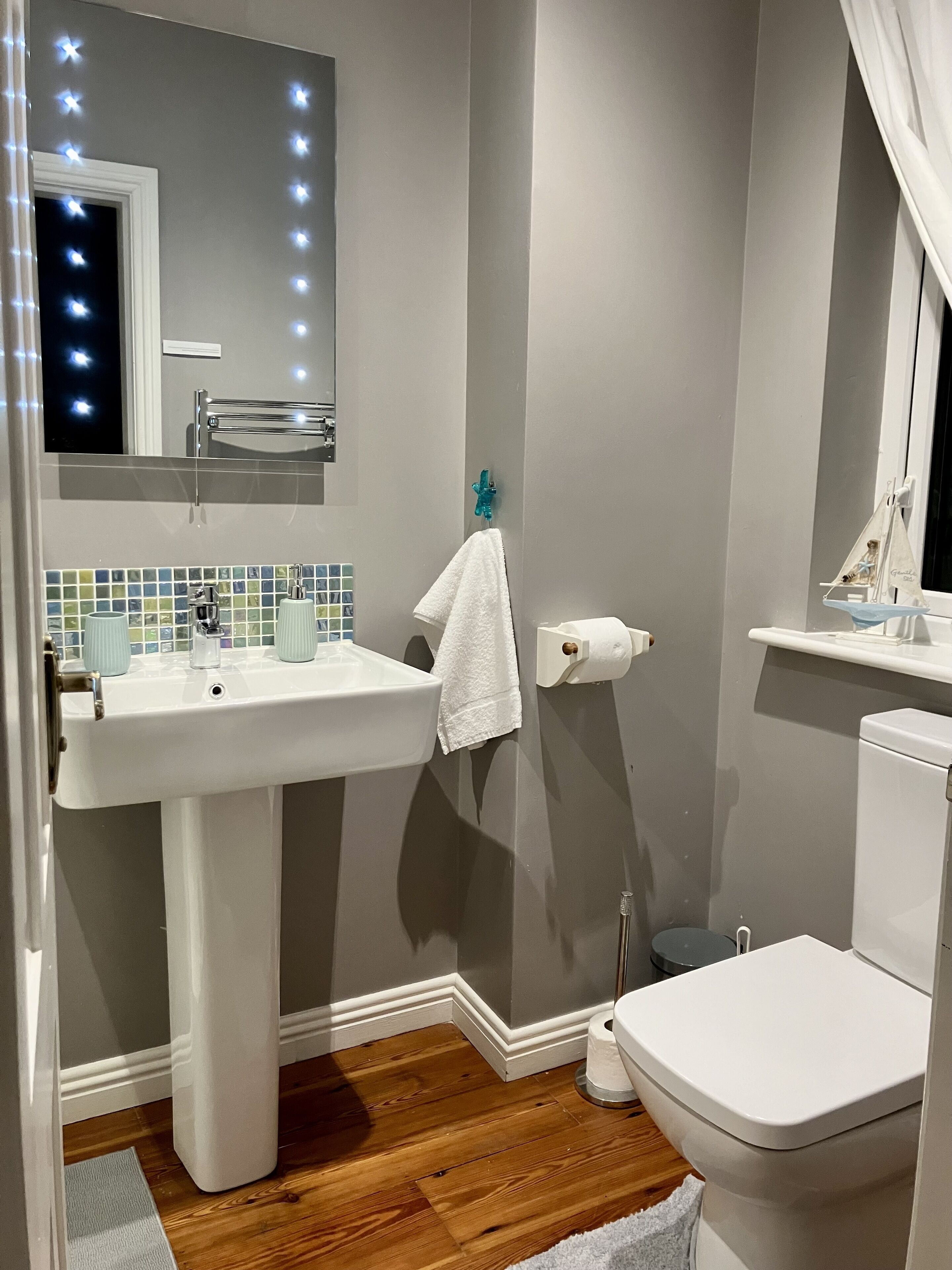 A bathroom with a white sink, toilet, and a mirror with lights.