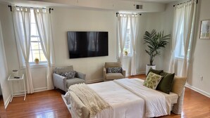 Quarto com cama grande, duas poltronas, televisão e planta em vaso.