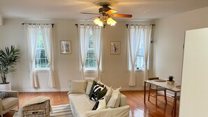 Uma sala de estar espaçosa com um sofá branco, uma mesa de jantar e um ventilador de teto.