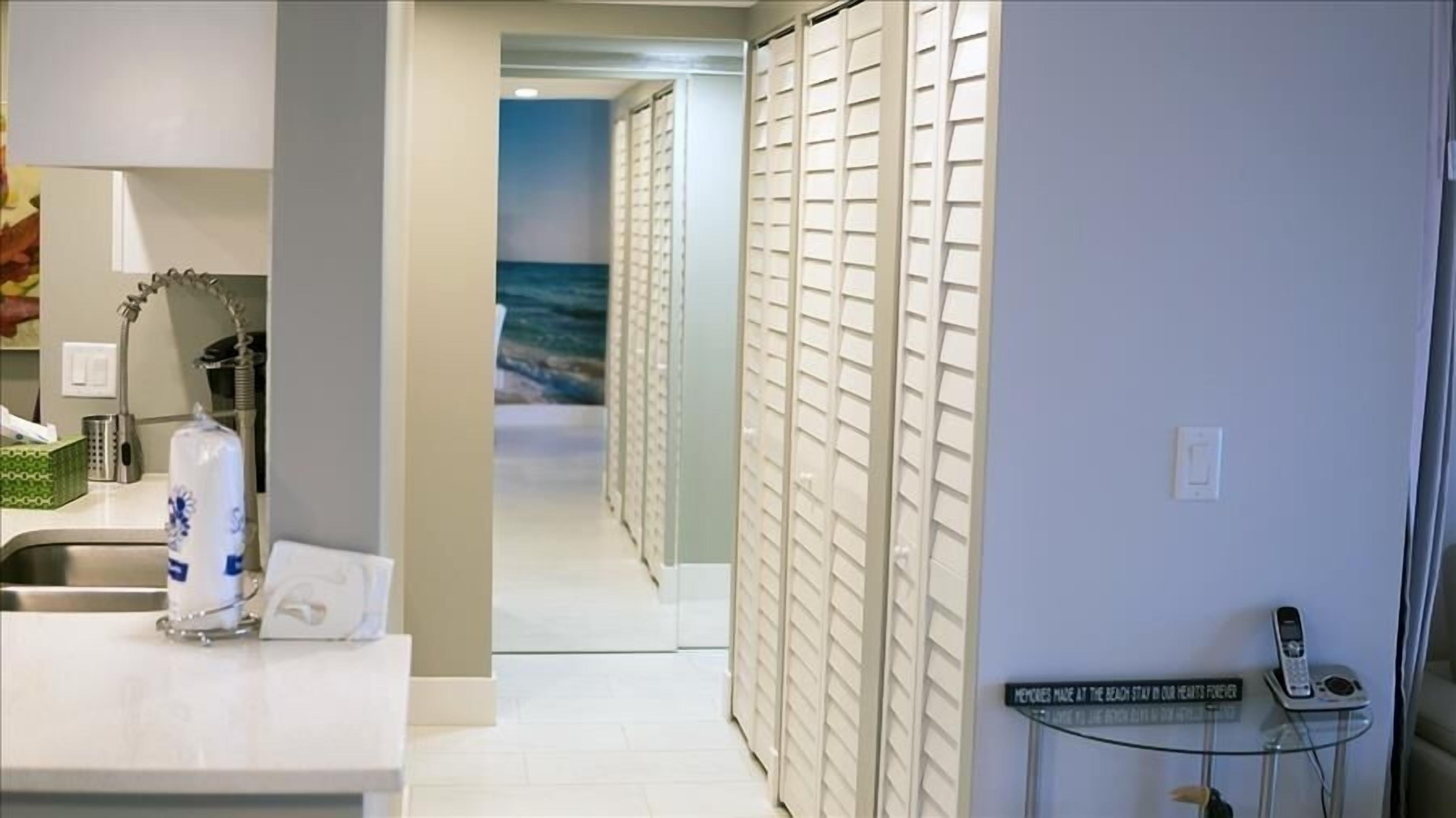 Ein Hotelkorridor mit Blick auf den Ozean durch eine Glastür, ein Waschbecken mit Pflegeprodukten und ein Telefon auf einem kleinen Tisch.