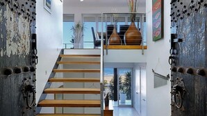 En modern inredning med en trätrappa som leder upp till ett andra våningsplan, en glasdörr och utsikt över omgivningen.