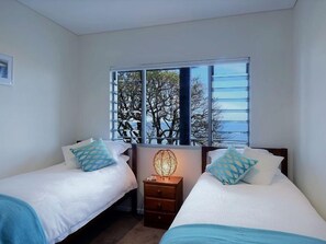 Une chambre avec deux lits, une fenêtre donnant sur les arbres et une table de chevet avec une lampe.