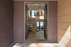 A modern interior with a staircase leading to an upper level, a view of the outdoors, and a door with a decorative metal gate.