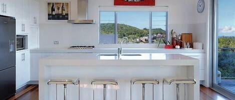 Una cocina moderna con una isla grande, taburetes de bar, un refrigerador de acero inoxidable y vistas al exterior.