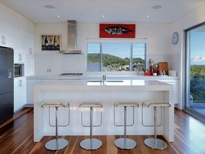 A modern kitchen with a large island, bar stools, a stainless steel refrigerator, and a view of the outdoors.