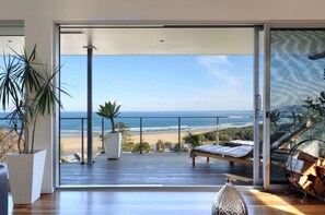 Uma varanda moderna com deck de madeira, uma cadeira de estar e vista para a praia e oceano.
