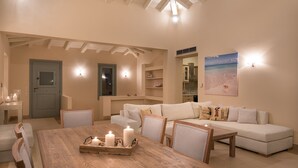 A spacious living area with a wooden dining table, white sofas, and a large painting of a beach scene. - Villa Gold in Petrothalassa (Porto Cheli)