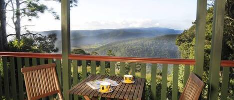 Eine Holzterrasse mit Tisch und Stühlen, mit Blick auf ein bewaldetes Tal und einem nebelverhangenen Hintergrund.