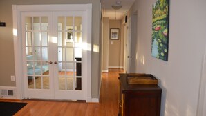 A hallway with a wooden floor, a white door with glass panels, a wooden dresser, and a painting on the wall. - Modern 3BR/2BA, Free parking, 9 miles to DC, minutes to 395-495 (Alexandria)