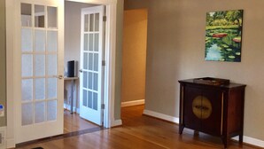 A room with wooden flooring, a door with frosted glass panels, a small wooden side table, and a painting on the wall. - Modern 3BR/2BA, Free parking, 9 miles to DC, minutes to 395-495 (Alexandria)