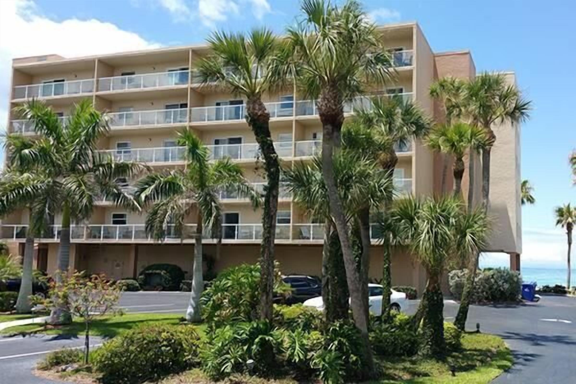 A multi-story hotel with balconies, surrounded by palm trees and a parking lot.