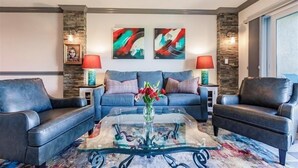 A living room with a blue sofa, two armchairs, a glass coffee table, and abstract paintings on the wall. - Beachcomber unit 303 (Longboat Key)