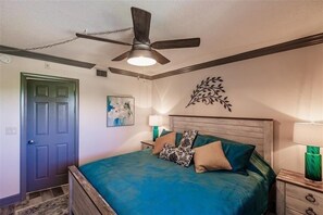 A bedroom with a bed, a ceiling fan, a door, and a wall decoration. - Beachcomber unit 303 (Longboat Key)