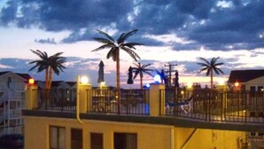 A beachfront property with a gated entrance, palm trees, and a sunset sky. - NEW! Beach Chic-Pool-triple bunks-Slps 7-beach chairs & cart-elev-off BW (North Wildwood)
