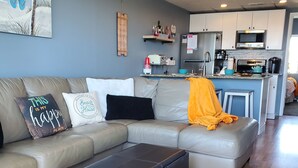 A modern living room with a sectional sofa, a black ottoman, and a colorful rug. - NEW! Beach Chic-Pool-triple bunks-Slps 7-beach chairs & cart-elev-off BW (North Wildwood)