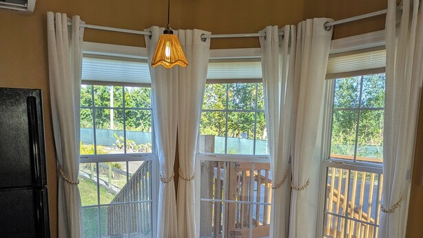 Un comedor con una mesa y sillas, una pequeña planta en maceta y tres ventanas con cortinas.
