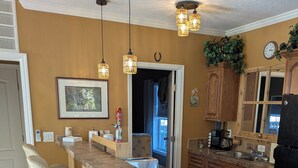 Una cocina con una isla central, taburetes de bar, iluminación colgante, armarios de madera y un bote de basura de acero inoxidable.