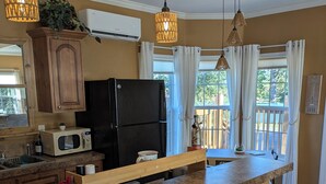 Una cocina con un refrigerador negro, un microondas y una encimera de madera. Hay luces colgantes y una ventana con cortinas.