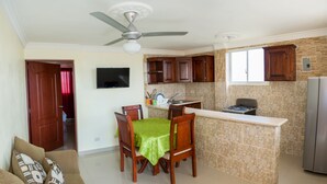 Una cucina compatta con zona pranzo, ventilatore a soffitto, televisore a parete e frigorifero.