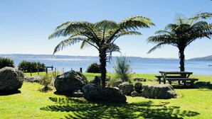 Et roligt udendørsområde med et picnicbord, store sten og palmer ved vandet.