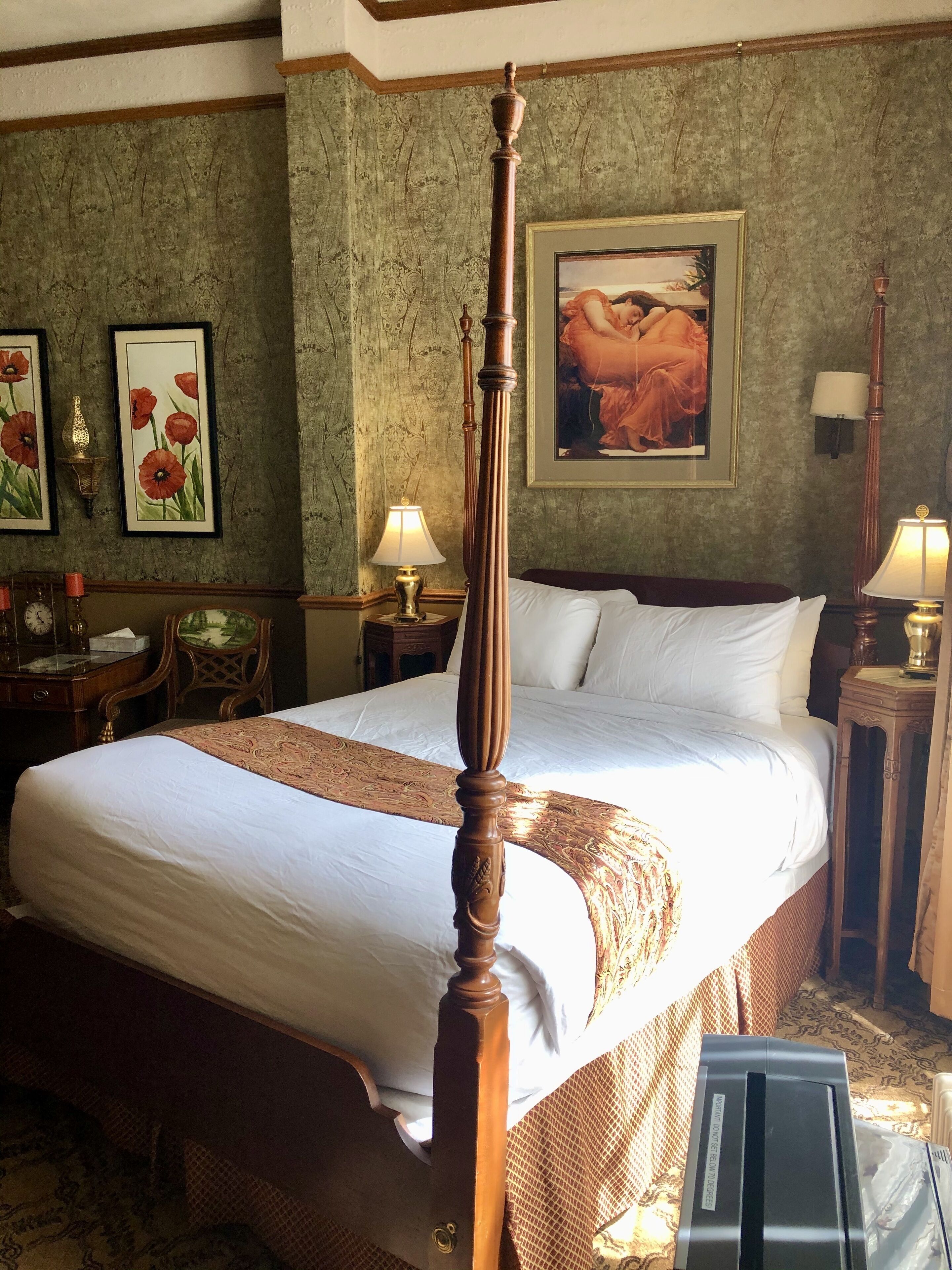 A four-poster bed with a wooden headboard, a large painting above it, and a clock on the wall.