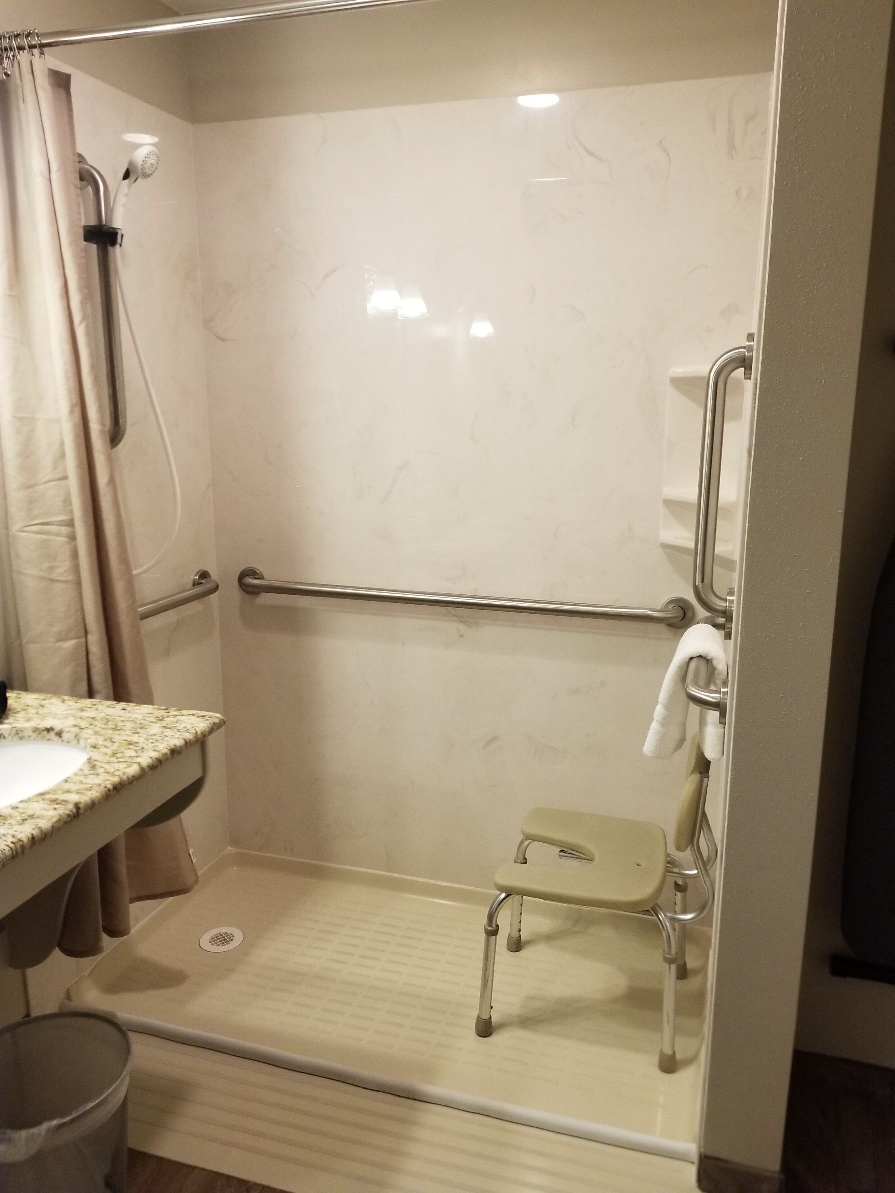 A bathroom with a shower, grab bar, toilet, and sink.