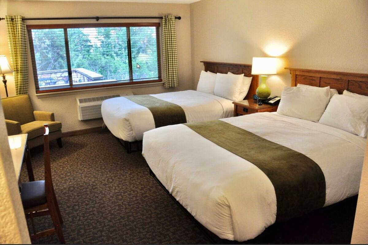 Habitación de hotel con dos camas, un escritorio, una silla, una ventana con cortinas y una lámpara de noche.