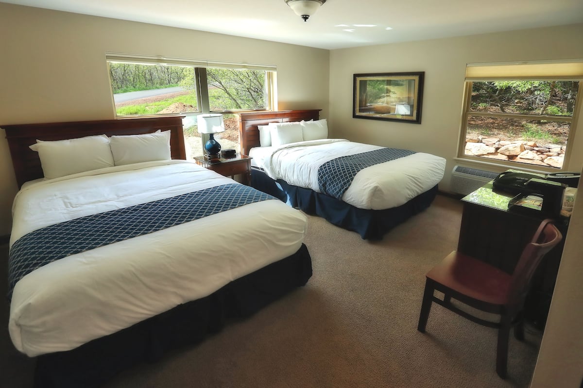 Habitación de hotel con dos camas, un escritorio, una silla y grandes ventanales con vistas al exterior.