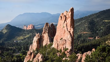 Un paisaje montañoso con formaciones rocosas destacadas y una vista distante de un valle con edificios dispersos.
