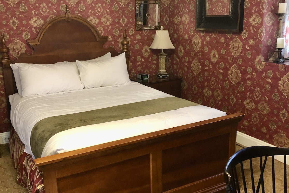 Un dormitorio tradicional con una cama de madera, una mesita de noche con lámpara y un espejo en la pared.