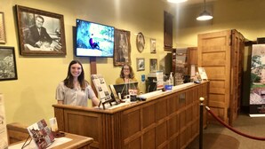 A reception desk with framed pictures on the wall, a television screen, and a wooden counter. - Glen Eyrie Castle & Conference Center A Ministry of the Navigators (Colorado Springs)