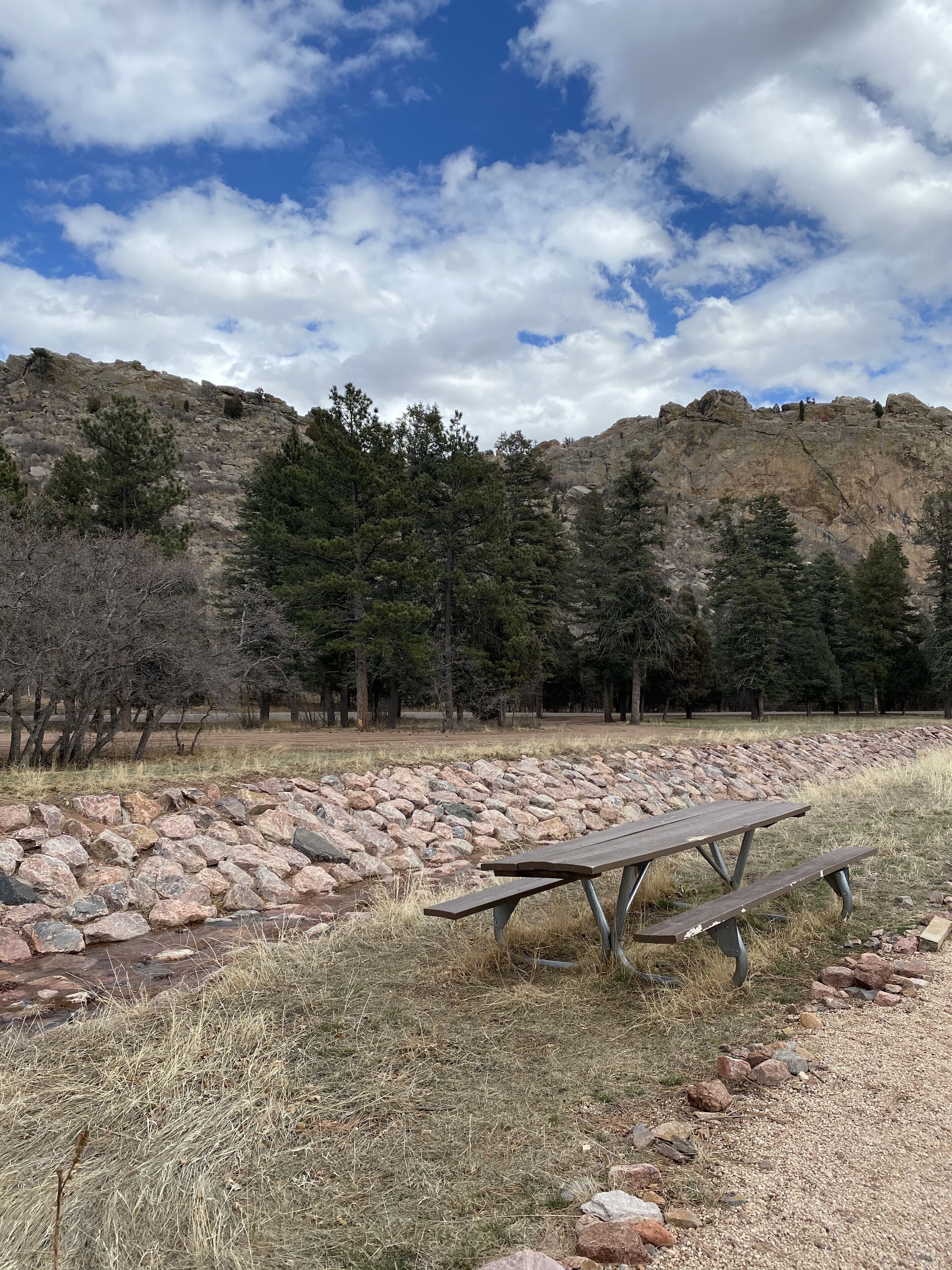 Une table de pique-nique installée dans un cadre naturel, avec une colline rocheuse et des arbres en arrière-plan.