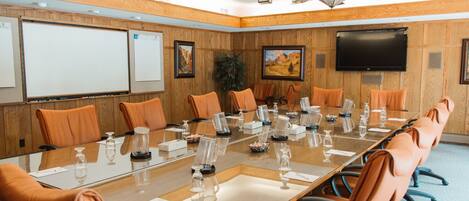 A conference room with a long table, multiple chairs, a flat-screen TV, and wooden paneling.