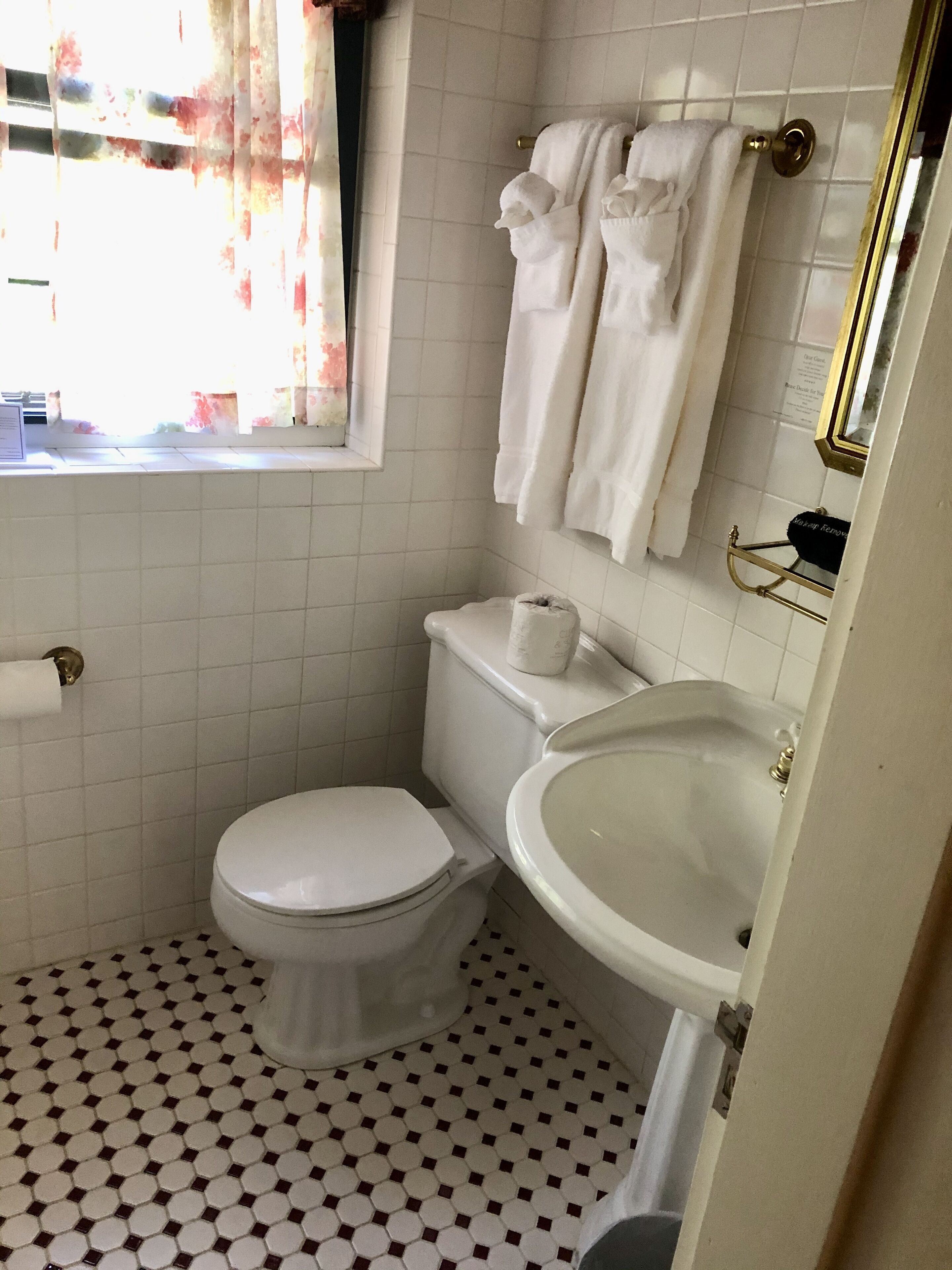 Une salle de bain avec des toilettes, un lavabo et une fenêtre avec des rideaux.