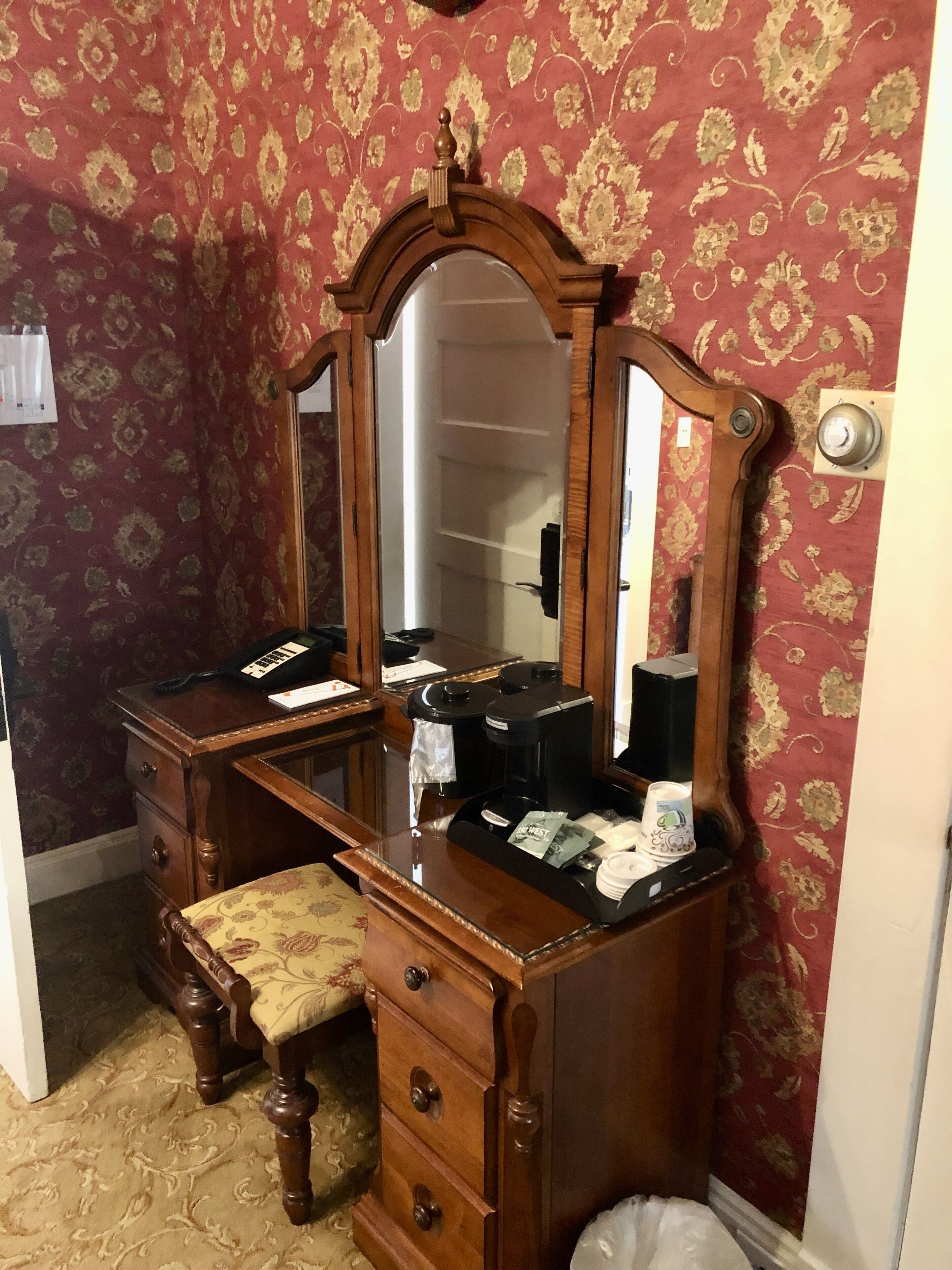 A wooden vanity with a mirror, a coffee maker, and toiletries.