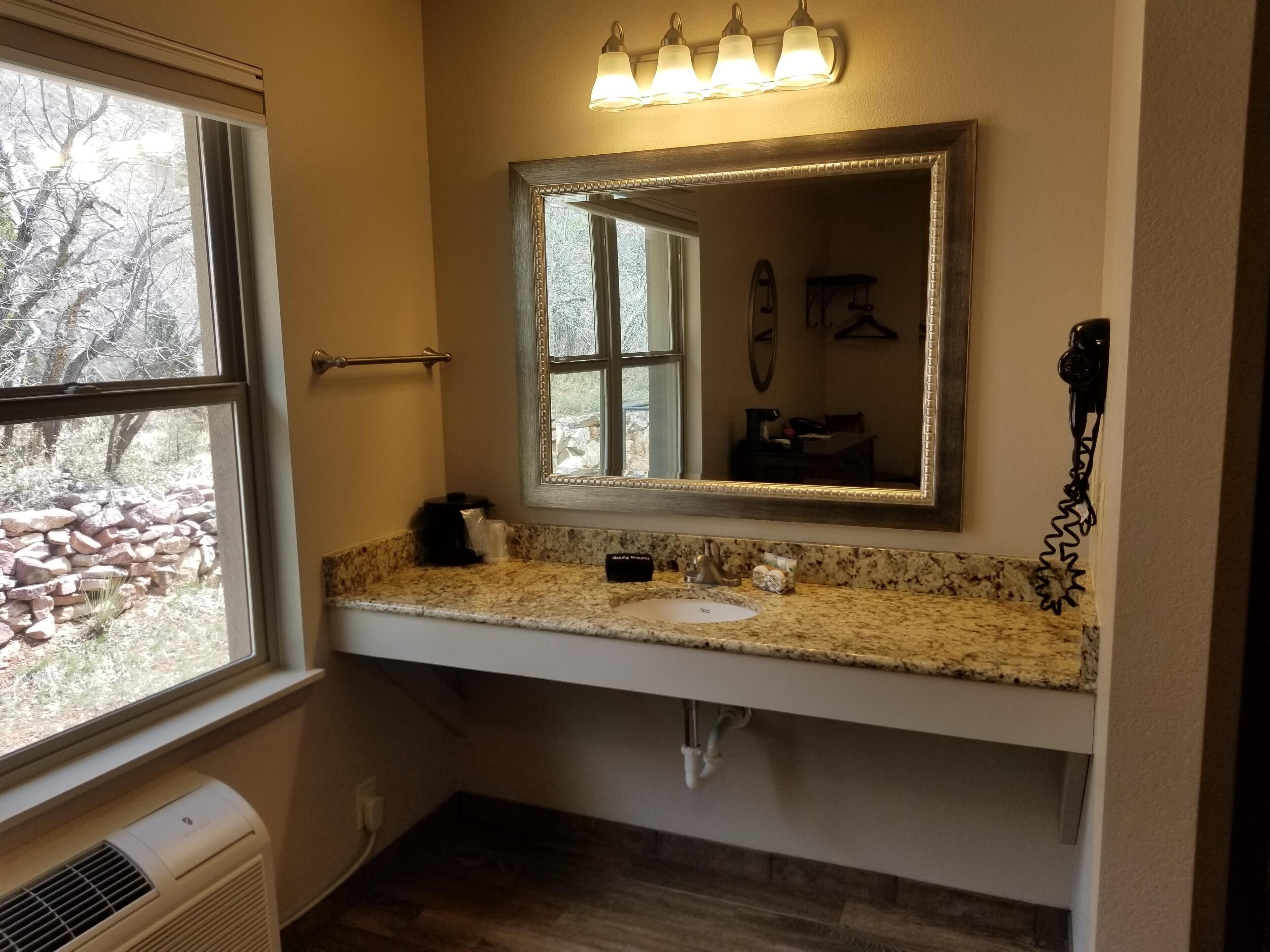 A bathroom with a large mirror, a sink, and a window.