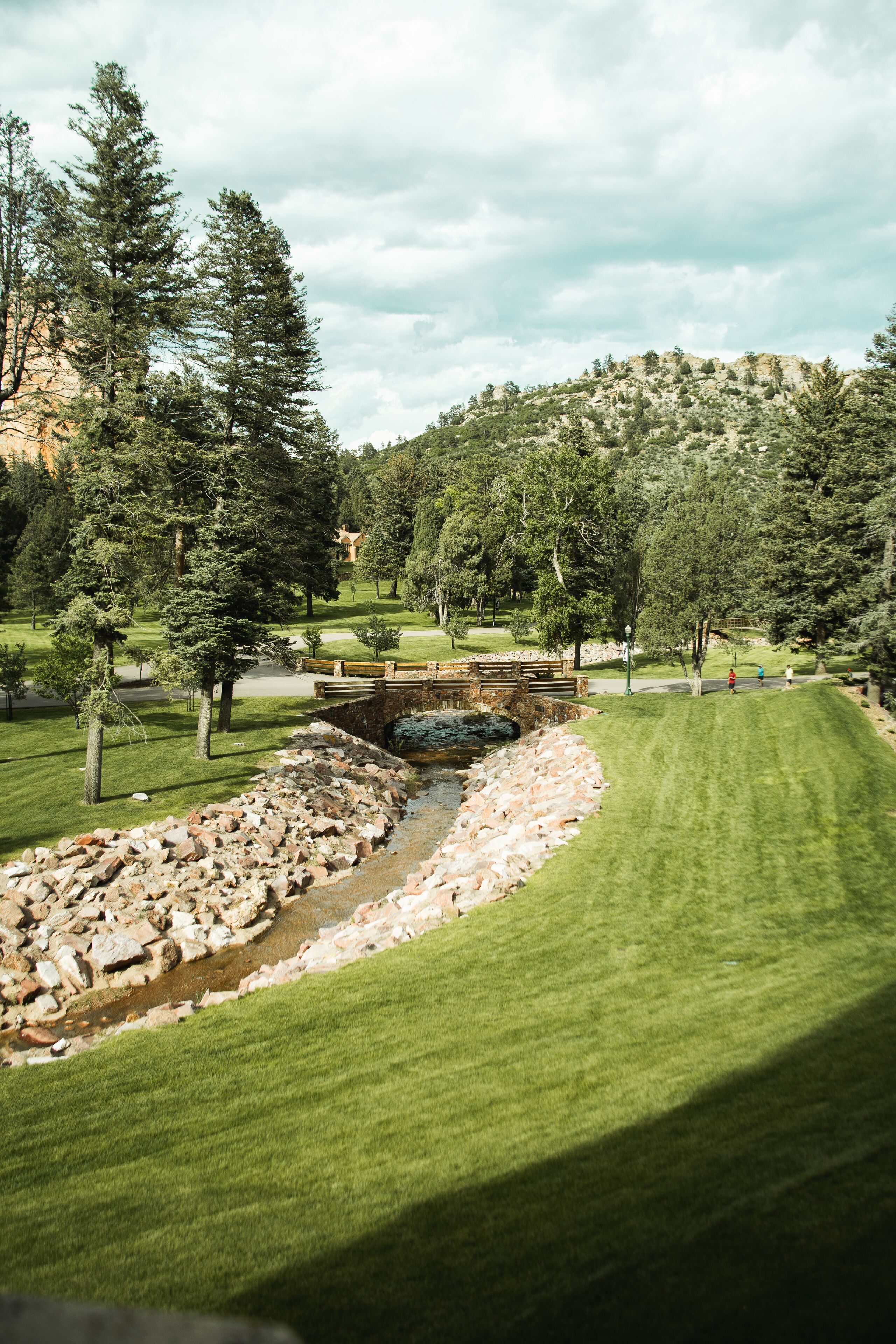 Un parcours de golf avec un ruisseau, des arbres et une montagne en arrière-plan.