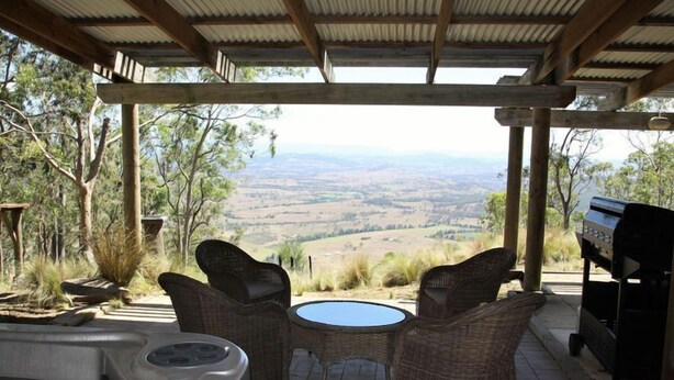 A covered outdoor seating area with wicker chairs and a hot tub, overlooking a scenic valley. - The gallery - eco-friendly atmosphere (Vacy)