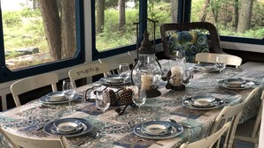 Une table à manger dressée avec des assiettes, des verres et des bougies, donnant sur une zone boisée.