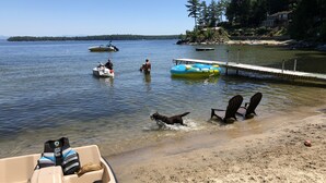 Une plage avec un bateau amarré sur le sable, un ponton flottant et une maison en arrière-plan.