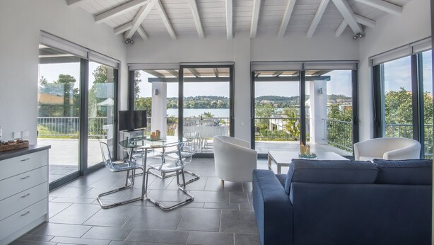 A spacious living area with a modern design, featuring a large sofa, a dining table with chairs, and a view of the outdoors through large windows. - Minimal Maisonette In Porto Cheli (Porto Cheli)