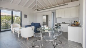 A modern kitchen with white cabinets, a dining area with a glass table and chairs, and a balcony with a view of greenery. - Minimal Maisonette In Porto Cheli (Porto Cheli)
